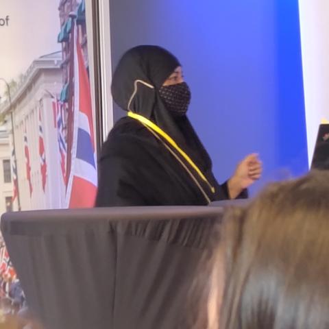 Shaharima Parvin at the EASE conference podium. She is a south Asian woman, wearing a black hijab and a black and yellow spotted face covering.