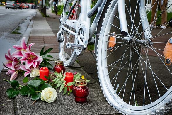 Weißes Fahrrad am Straßenrand mit Blumen davor.