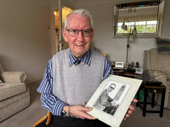 David at home holding a photograph of his younger self in front of the Guildhall - one of Swansea's iconic clocks he once maintained