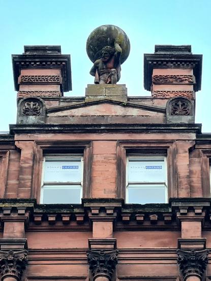 A statue of Atlas carrying the world on his shoulders on the top of a Victorian building in Glasgow.
