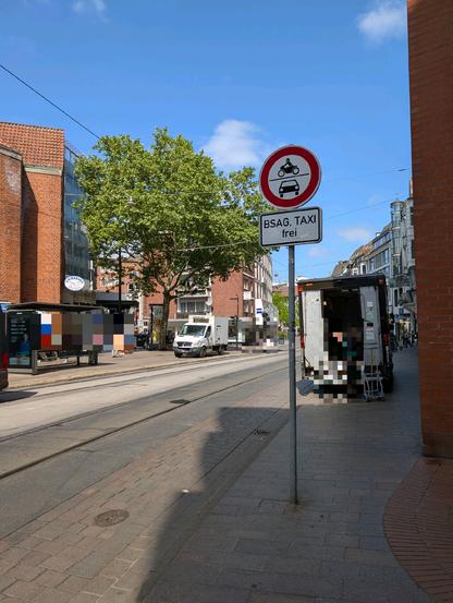 "Einfahrt verboten"-Schild. Direkt dahinter ein Lieferwagen auf dem Gehweg. Auf der anderen Straßenseite parkt ein Lieferwagen auf der Straßenbahnhaltestelle.