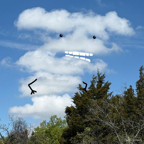 A photo of some green tree tops with a blue sky and vertical stacked cloud above. The cloud had gaps for a mouth and eyes, which I have subsequently drawn on along with some arms. It looks like it has a wide, heavy (and indeed fluffy) furrowed brow.