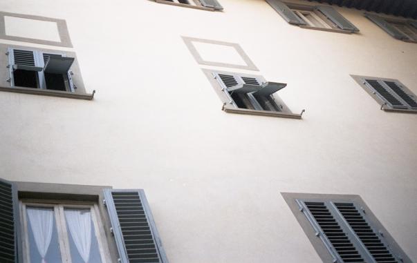 Shot looking up at a wall of windows with shutters in varying degrees of openness