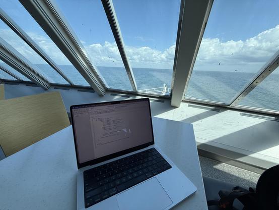 A picture of my laptop on a table in a ferry with the ocean in the background. Xcode is open on my laptop showing code of a feature I’m working on for Zenitizer.