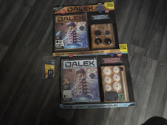 The image features two packages of a "Dalek" build kit from "Doctor Who." Each kit includes components for building a remote-controlled Dalek with movement, lights, and sound effects. There’s also a promotional card with a TARDIS design