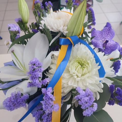 Un bouquet de fleurs blanches et violettes plus deux rubans jaunes et bleus en femmage à Anzhela qui était de nationalité ukrainienne.