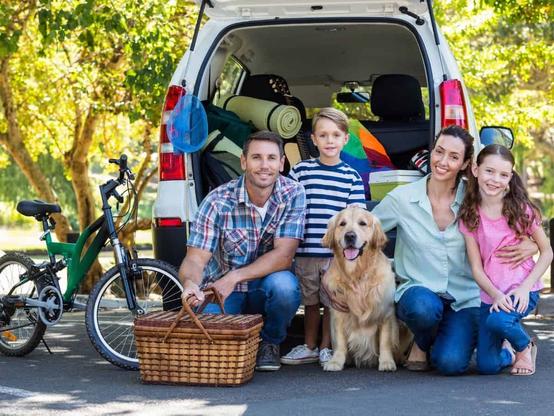 A family kneels behind a vehicle loaded with gear for their summer vacation.
