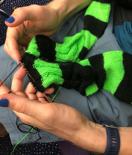 Two striped socks (black and neon green) being knit simultaneously. The stripes are "mirrored", so the stripe being green on one sock is green while it's black on the other.