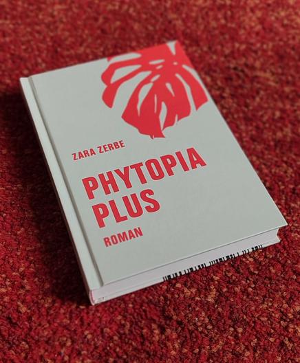 Auf einem rötlichen Hintergrund liegt ein graues Hardcoverbuch mit roter Schrift und Grafik: Zara Zerbe Phytopia Plus.