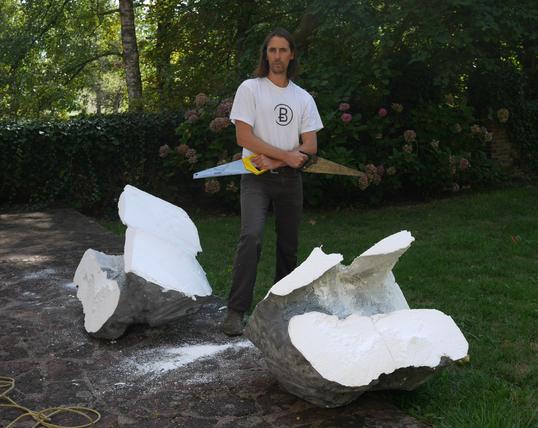 A man with two sows in each hand, standing up between two massive pieces of fake polystyrene rocks.