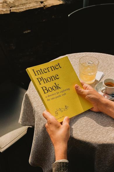 The Internet Phone Book with its yellow cover, held by hands above a café table on a sunny day.