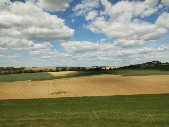 Farmland with green bits, yellow bits, a lot of blue and some fluffy white bits.
