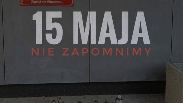 Zdjęcie ściany komisariatu ze zniczami pod nim. Na środku zdjęcia napis 15 maja nie zapomnijmy