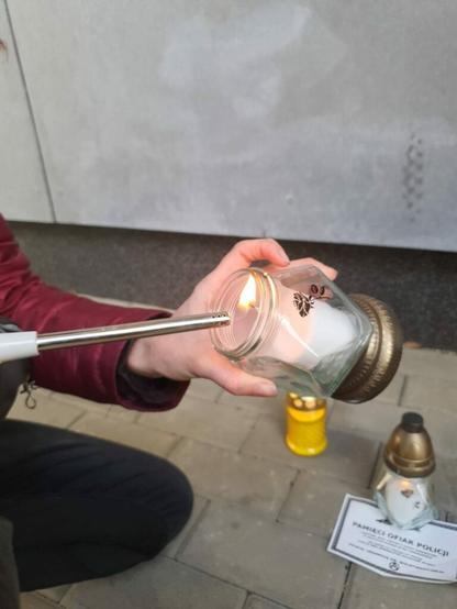 Zdjęcie przedstawia osobę zapalającą znicz.