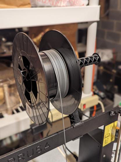 an almost-empty spool of gray PLA feeding down to a Prusa 3D printer that you can just see the top of
