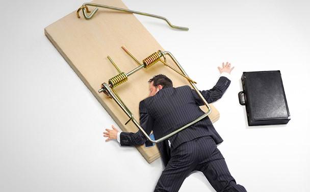 A guy in a business suit caught and crushed in a human sized mouse trap (a human trap) and his briefcase fell next to him
