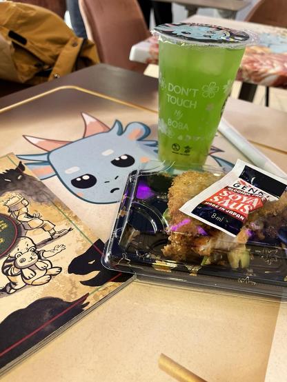 A packed sushi sandwich and some shiny green ice tea on a table with a cute Managua-style dragon. Oh, and a bit of printed edition of Yokai Hunter Club.