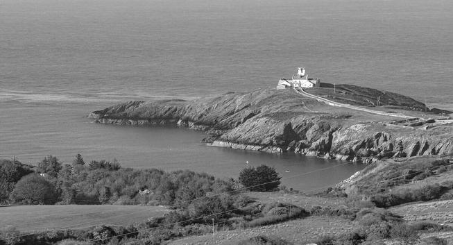 A panoramic view of the sea from above. Below, an arm of land juts out into the water. Here you can see a white lighthouse.