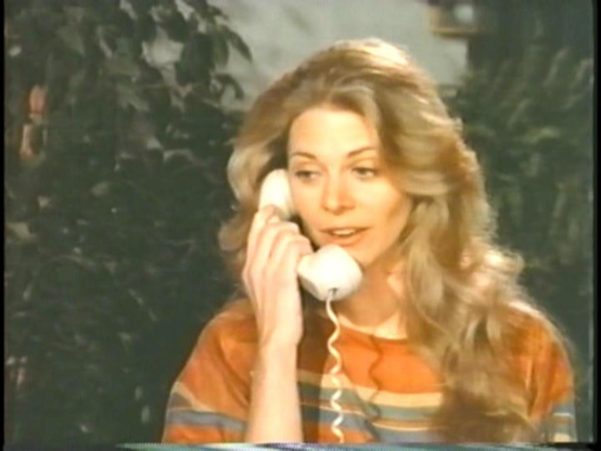 Lindsay Wagner in the 1983 TV movie, "Two Kinds of Love."  She is shown from the shoulders up, wearing a horizontally striped sweater, of orange, brown and blue.  Behind her is some greenery, perhaps vines or trees.  She is holding a white phone receiver to her ear and has a pleasant look on her face.  Her curly blond hair hangs down below her shoulder.