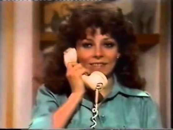 Actress Marcia Gomez, in a still from "The Rich Also Cry," is in an interior setting, with brightly striped wall paper behind her.  She has a white phone receiver to her ear in a closeup shot that only includes her head and shoulders.  She is wearing a teal blouse and her dark, curly hair falls around her shoulders.