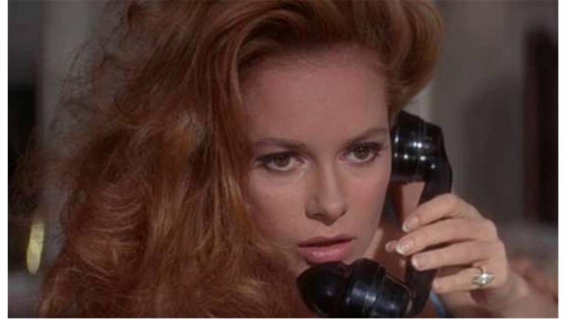 In a still from the Bond movie, "Thunderball,"  Luciana Paluzzi is shown in a very close up image of her face only.  She is holding a black phone receiver to her ear and she seems involved in a conversation.  Her long, red, curly hair is hanging down toward her shoulder.