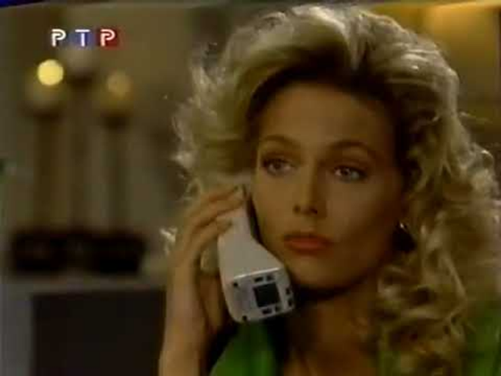 In a screencap from the soap opera "Santa Barbara" Nina Arvesen is holding a white cordless phone in a close up shot, with just her face visible.  She is in an interior setting, but the background is blurred.  She has the most gorgeous curly blond shoulder length hair.