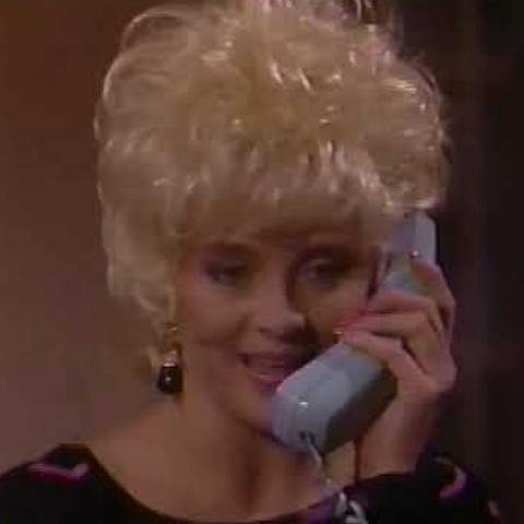 I could not find an identification for this actress, but I like her too much to leave her out.  She has curly platinum hair that is curled and shaped into a lovely dome.  She is facing the camera, shown from the shoulders up, holding a light blue princess phone receiver to her ear. She is wearing a purple velvet top and her nails are long and painted pink.