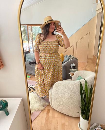 Caroline wears a yellow shirred block print dress and a Panama hat.