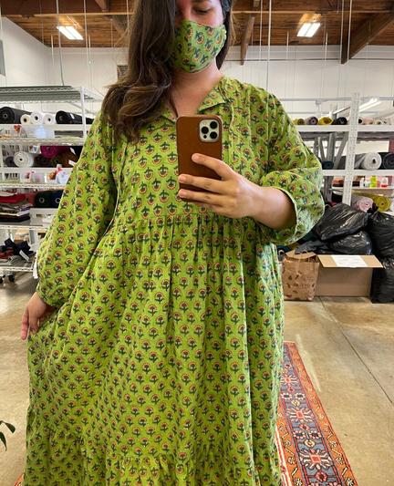 Caroline wears a long sleeved green block print dress with a gathered tier and a matching mask.