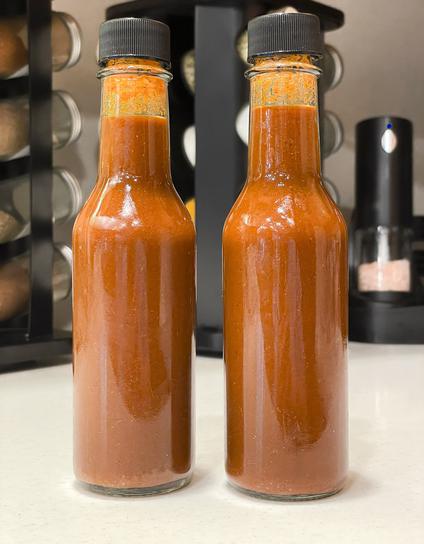 Two bottles of homemade red jalapeno hot sauce on a counter top in my kitchen