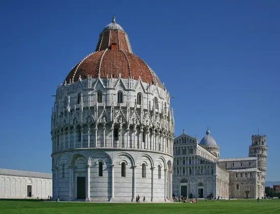 The image features a complex of buildings commonly associated with Pisa, Italy. It includes the Pisa Baptistery, which is distinguished by its round shape and unique architectural features. Adjacent to it is the Leaning Tower of Pisa, known for its unintended tilt, and the Cathedral of Santa Maria Assunta with its distinctive façade. The sky is clear, and the buildings are surrounded by a green lawn, showcasing their intricate designs and historical significance.

Image Credits: Wikimedia / Massimo Catarinella / CC BY-SA 3.0