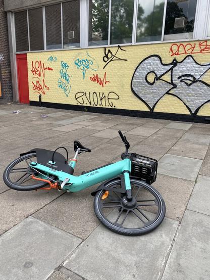 An e-bike lying on the ground, in front of a wall with graffiti