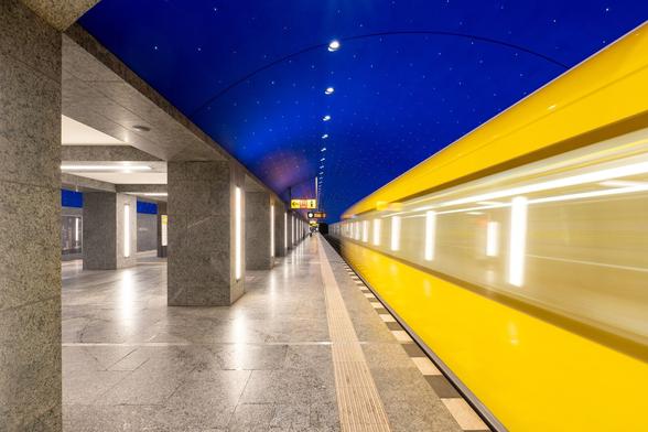 U-Bahnhof Museumsinsel. Die Säulen und der Fußboden des U-Bahnhofs sind in grauem Naturstein ausgeführt. Die Decke ist Blau mit kleinen Lampen gestaltet. Auf dem Gleis fährt eine gelbe U-Bahn der Linie 5 in Richtung Hauptbahnhof ein.