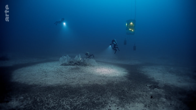 das bild zeigt eine unterwasseraufnahme im bereich natürlich geformter ringstrukturen, in der taucher und tauchroboter die umgebung und beschaffenheit genauer untersuchen