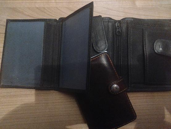Two wallets on a desk. One wallet is brown and small. Its outside is made of leather, and is metal on the inside. it is meant to hold cards that can be pushed out using a mechanism on its metal frame. There is little room for anything else.

The small wallet is laying upon a bigger wallet. This one is black, also made of leather. It looks more old school, with room for pictures and has many places to put various items.