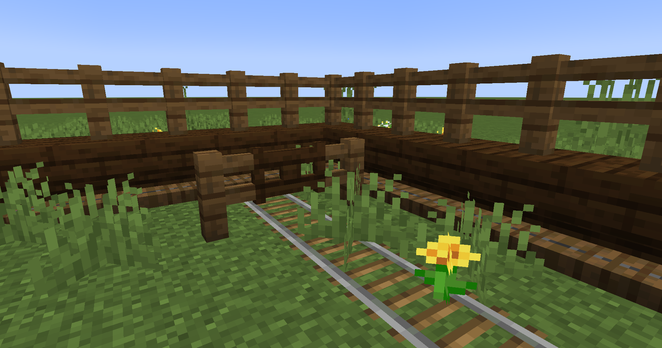 An in-game screenshot showing off a minecart rail under a fence gate, grass and a flower over this rail, and trapdoors under/inside upside down stairs.