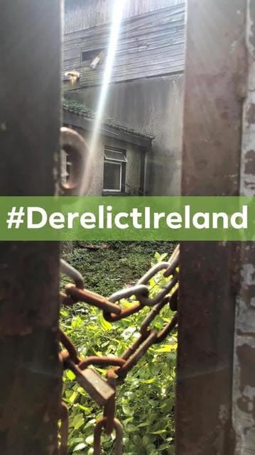 A derelict property in Cork City,  closed by a rusty chain with the tag #DerelictIreland across and a sun ray leaking through