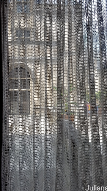 A view from inside Biltmore, through an open weave curtain toward a wing of the mansion that forms a courtyard.