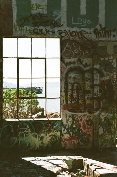 Light streams through an open window casting light in a graffiti tagged abandoned ferry landing warehouse.