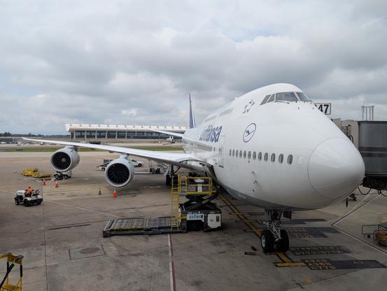 One of Lufthansa's Boeing 747-8 jets sits parked at gate B47 at Dulles Airport, with IAD's main terminal visible behind it.