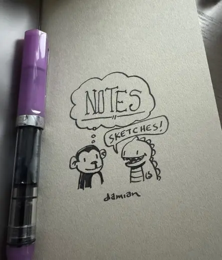 A photo of a notebook  cover next to a purple fountain pen. There is a drawing of a cartoon monkey thinking "notes" facing a cartoon Zilla saying "sketches"