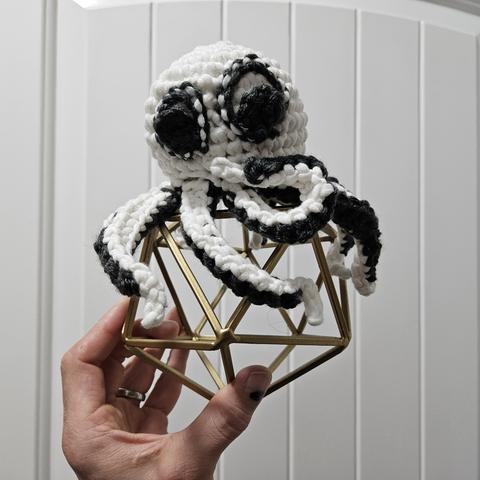 an amigurumi octopus of white and dark grey. it has crochetted googly eyes.
