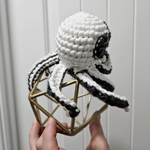 a side view of a crochetted octopus whote and dark grey on a skeleton of an icosahedron.