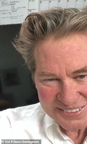 Older Val Kilmer smiling at the camera with chubby red cherub cheeks and gray hair