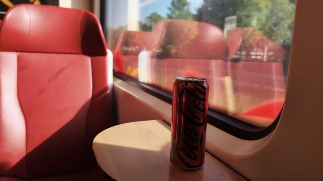 Photo of a coca cola zero can in front of the window in a driving train with red seats.