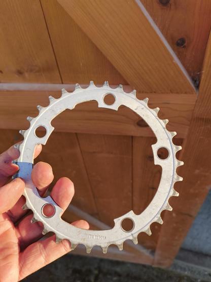 A hand holding a bent bicycle chain ring
