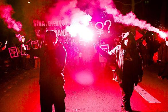 Un manifestation de nuit avec des fumigènes roses. On distingue le mot SIDA sur une banderole.