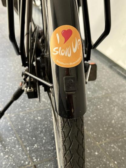 Blick von hinten auf mein Stadtrad. Unten am Schutzblech ist ein Aufkleber „I love slowUp“. Diesen gibt es am Anlass, so dass ich ihn regelmäßig erneuern kann, wenn er von Wind und Wetter verblichen ist. Er ist die einzige Deko am sonst sehr schlichen Rad.
