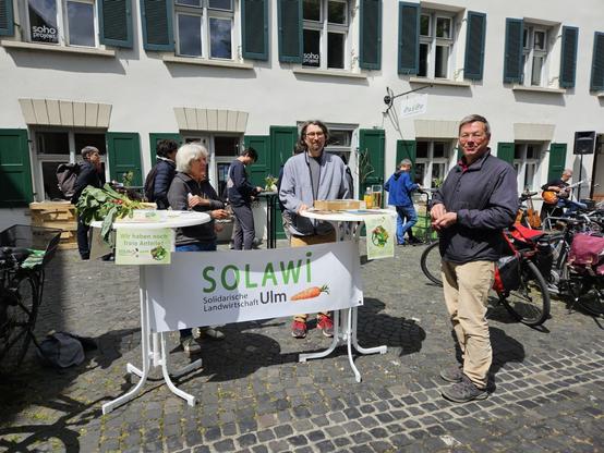 Drei Personen stehen am Solawi-Infostand bei bestem Wetter!