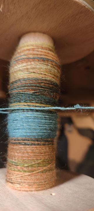 A bobbin containing some spun single in brown, blue, orange and dark green tones